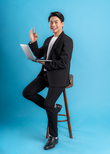 Full body Young business man wearing a vest using laptop and posing on a blue background