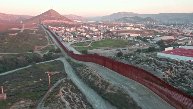 International Border Wall Between Tecate California and Tecate Mexico Near Tijuana Baja California Norte at Dusk Under Stunning Sunset with View of the City From the USA