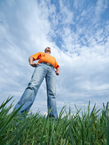 Outdoor wide-angle portrait of a tall man in jeans on blue sky and green grass background