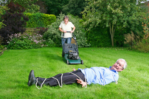 wife pushing lawn mower towards roped up husband who is laying on the the lawn