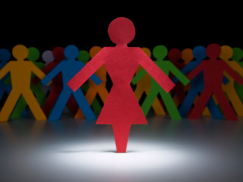A female paper figure stands under the spotlight in front of multicolor crew.