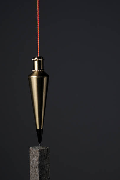 Plumb-bob over survey post The is plumbline, blumb-bob, or plummet on dark grey with orange string hanging over a stake. This represents precision. plumb line stock pictures, royalty-free photos & images