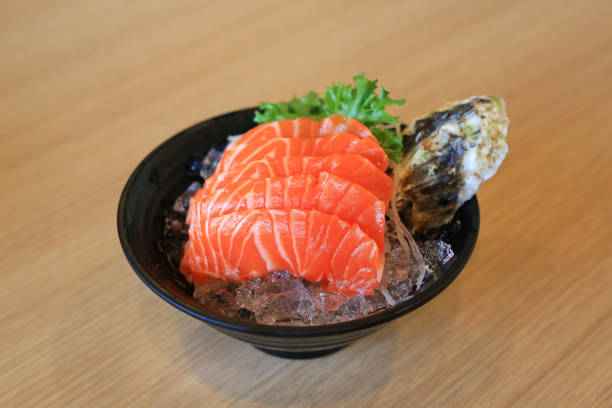 лосось нарезает филе сашими на льду в черной чаше на фоне деревянного стола. традиционная японская кухня. - pacific salmon стоковые фото и изображения
