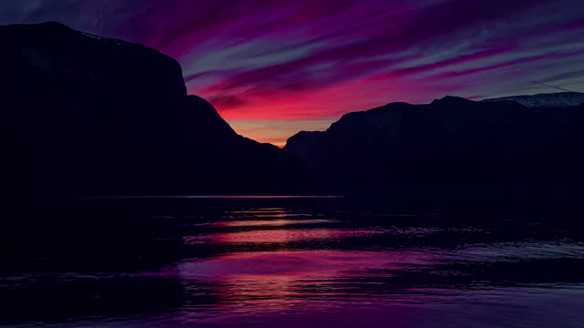 Brilliantly colorful sunset time lapse at a mountain fjord in Norway as the water shifts with the tide, wind and currents