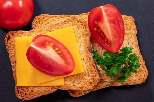 Three Biscotti Crackers, Cheddar Cheese, Tomatoes and Curly Parsley on Black Background