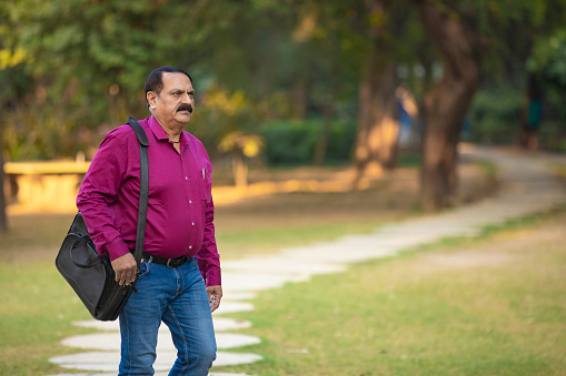 Indian man holding laptop bag and walking at park.