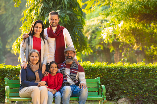 happy Indian family sitting at park in winter wear or warm clothes.