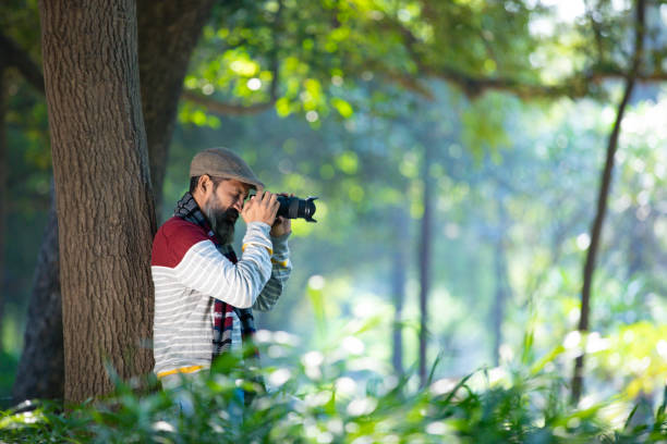 Young traveler man sitting on top of the mountain and taking a picture of a beautiful landscape of Bir billing mountain hills with dslr camera.