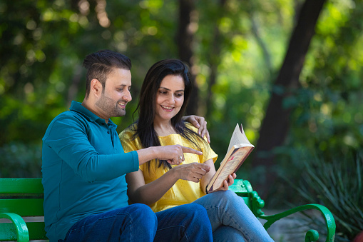 Young indian man and woman reading book at park.