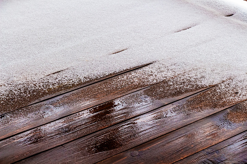 Snow melts on the wooden floor of the open veranda of a private house.