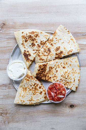 Chicken quesadilla cut in four pieces and served on a silver plate on a wooden table.