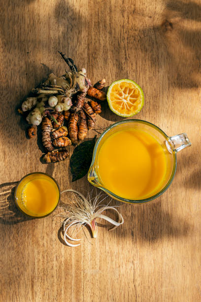Ginger and orange juice served in a pitcher and in a glass on a wooden table.