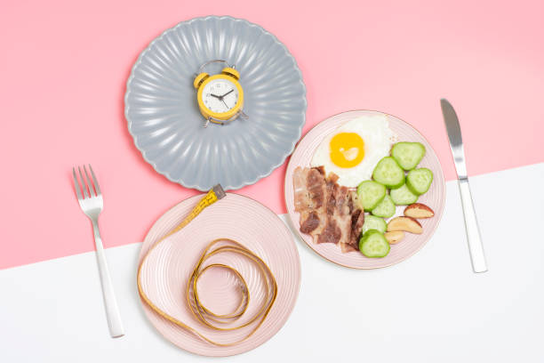 ピンクと白の背景に食べ物、目覚まし時計、測定テープの上面図、断続的断食のコンセプトを持つプレート。 - diet pill ストックフォトと画像