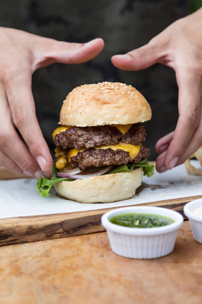 istock Hand holding a whole hamburger, on a restaurant table. Delicious and nutritious food. 1468118046