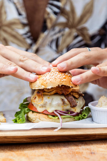 istock Hand holding a whole hamburger, on a restaurant table. Delicious and nutritious food. 1468118100