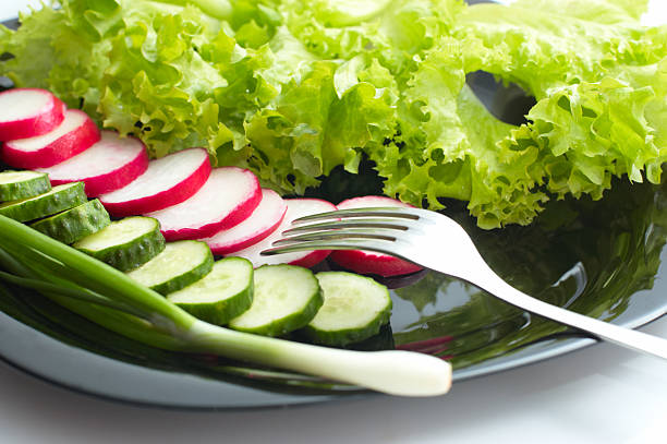 Vegetarian diet. Fresh cucumber, radish and Lettuce on black plate. Focus on fork.