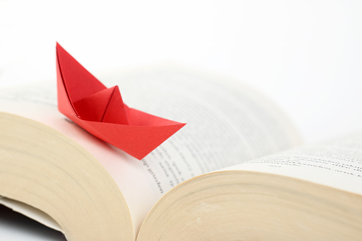 Origami red paper boat floating on the pages of a book.  Learning, education, reading, knowledge concept