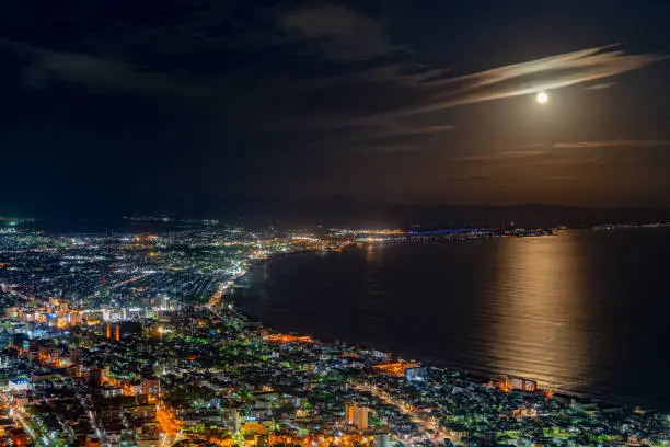 Photo of Hakodate City night view from Mt. Hakodate observatory, big bright moon light up the sea, golden reflection on surface