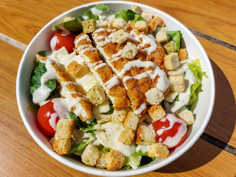Caesar Crispy Chicken Salad on table in a fast food restaurant that includes crispy breaded chicken breast pieces, lettuce, cherry tomatoes, shredded cheese and garlic-herb flavoured croutons