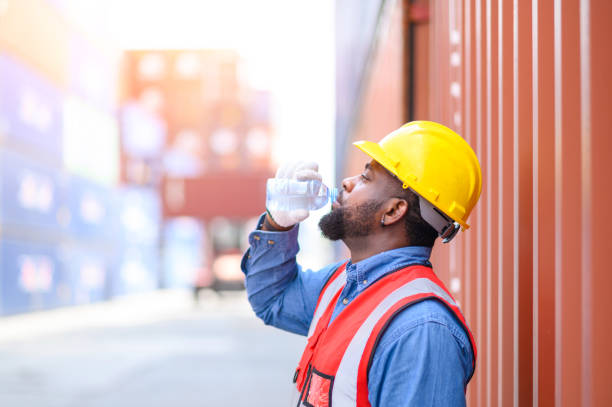 logistic staff workers wearing reflective vests and white helmets in shipping container yard, Drinking water when resting after working. Cargo Ship Import Export Factory Logistic.