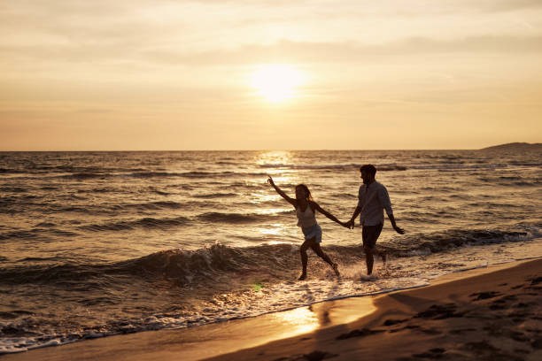 istock Playful couple running through sea on the beach at sunset. 1468134143