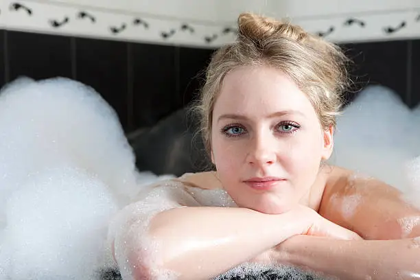 Young smiling woman enjoys the bath-foam in the bathtub.