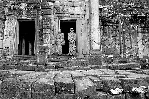 Cambodian monks doorway Bayon Angkor Thom Two Cambodian monks standing at a stone doorway at the outer terrace of lower levels of the ruins of the Bayon, Angkor Thom, Cambodia. black and white travel travel destinations monk stock pictures, royalty-free photos & images