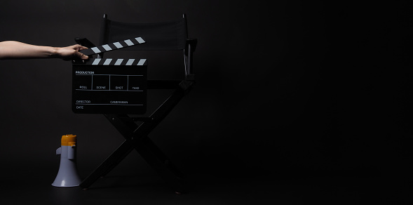 BlackDirector chair and magaphone and hand is hold Clapper board on black blackground.