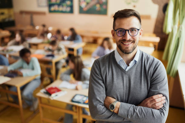 Happy elementary teacher in front of his students in the classroom. - fotografia de stock