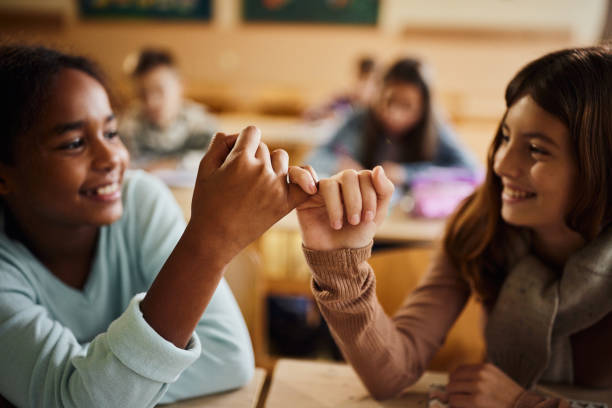 Reconciliation at school! Close up of happy schoolgirls reconciling with little fingers at school. pinky finger stock pictures, royalty-free photos & images