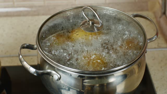 Gas home stove with potatoes boiled on it in a stainless steel saucepan with a transparent lid. The concept of cooking healthy food. Close-up