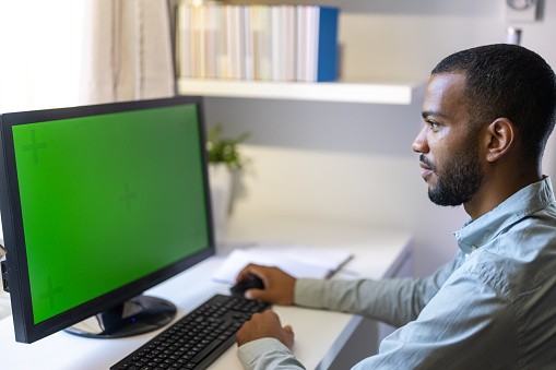 Close-up of man working on green screen of computer monitor in home office.