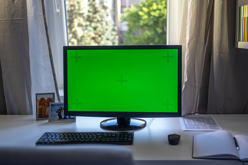 Green screen of computer monitor on desk in home office.