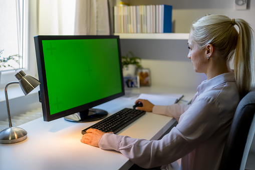 Close up of a blank computer screen standing on a white table in modern interior with big window with city view, mock up. 3D Rendering