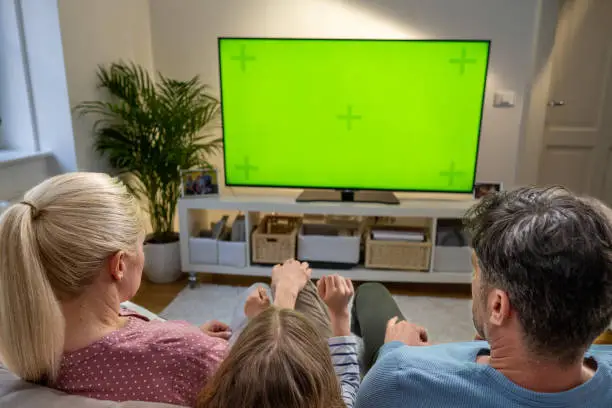 Family watching green screen of TV while sitting on sofa in living room.