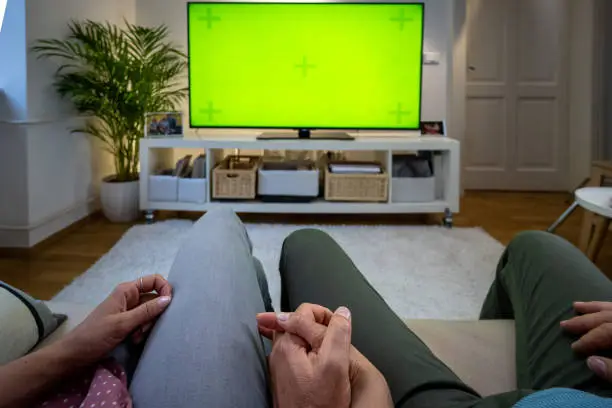 Mid section of couple watching green screen TV while sitting on sofa in living room.