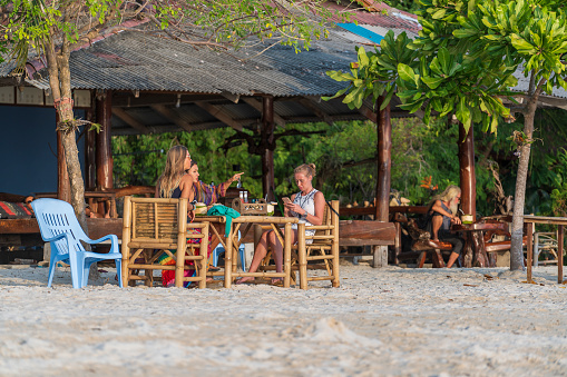 Koh Phangan, Thailand - Feb, 10, 2022 : Young european girls relaxing in beach cafe near the sea during sunset on the tropical island of Koh Phangan, Thailand