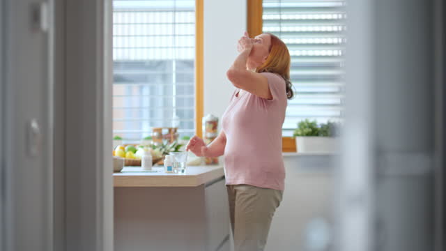 Senior woman taking her medicine in the kitchen