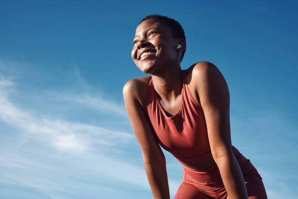 fitness, black woman and happy athlete smile after running, exercise and marathon training workout. blue sky, summer sports and run of a african runner breathing with happiness from sport outdoor - evento de pista imagens e fotografias de stock