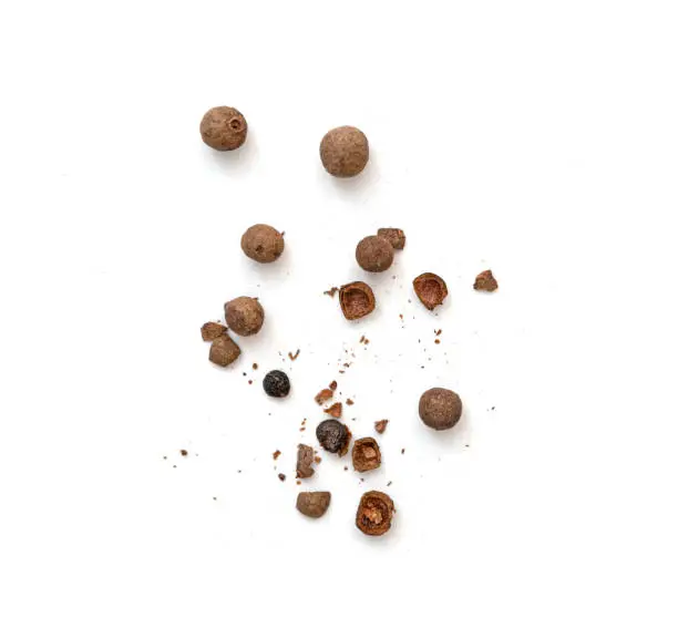 Mix of whole and broken pieces of black pepper, peppercorns or allspice isolated on white, top view
