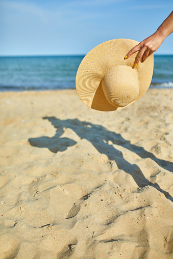 Woman hold in hand straw hat on yhe beach near sea, Summer vacation and travel. Copy space