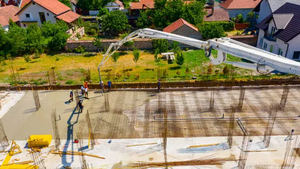 Photo of Above view rigger, worker is holding pump hose to pouring fresh concrete into building foundation over reinforcing steel bars