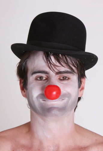 Portrait of a funny clown with black hut, red nose and white background