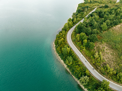 A car is driving on a road next to the lake shore. Aerial point of view.