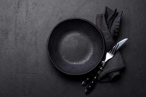 Empty plate with fork and knife on dark stone table. Flat lay with copy space