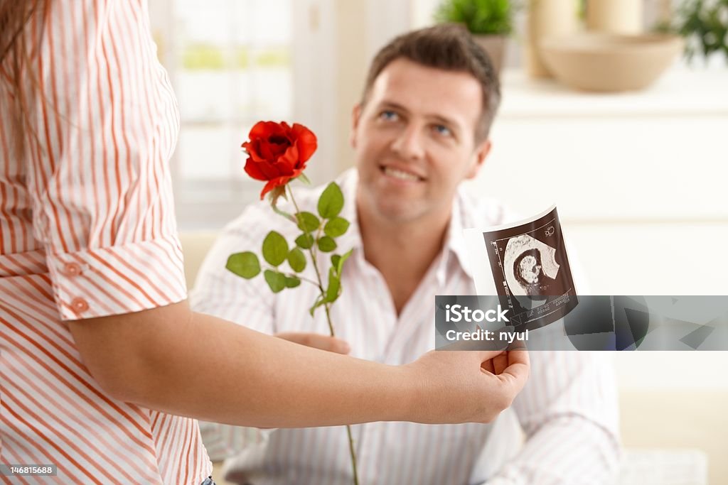 Man giving rose to pregnant woman Man giving red rose to pregnant woman holding ultrasound image of baby. 20-29 Years Stock Photo