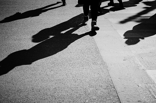 Pedestrians walking on zebra crossing throwing hard black shadow oh the road.
