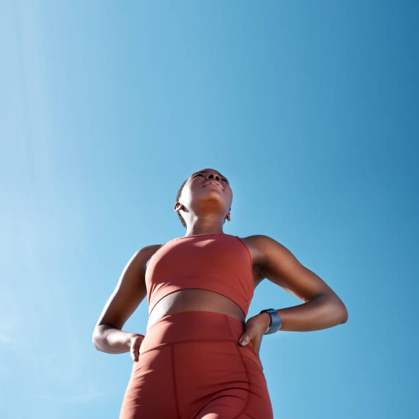 niedriger winkel, sportfitness und schwarze frau im freien, die sich auf training, training oder übung mit mock-up vorbereitet. blauer himmel, gesundheit und weibliche läufer, die an sport, cardio oder joggen für wellness denken. - endurance sport stock-fotos und bilder