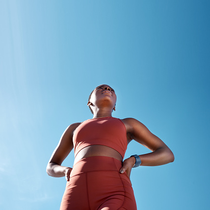 Low angle, sports fitness and black woman outdoor getting ready for workout, training or exercise with mock up. Blue sky, health and female runner thinking of exercising, cardio or jog for wellness.