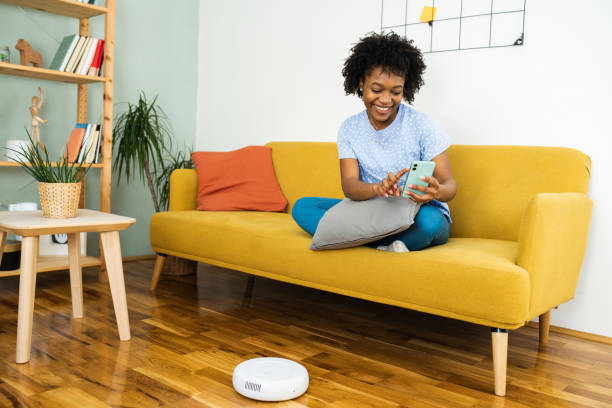 istock Happy woman using her smartphone and turning on robotic vacuum cleaner 1468165539